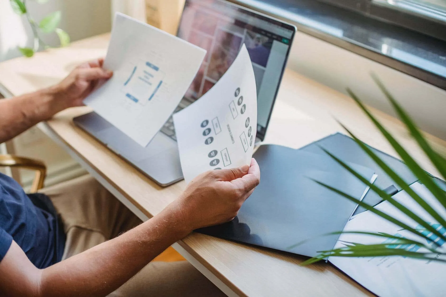 Hands holding printed wireframes in front of a laptop